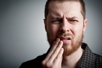 A man in pain holding touching his teeth